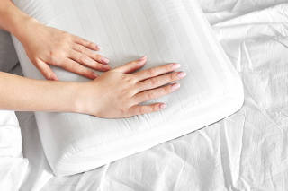 Female hands hold and show an orthopedic pillow on a white bed. Comfortable sleep and healthy spine