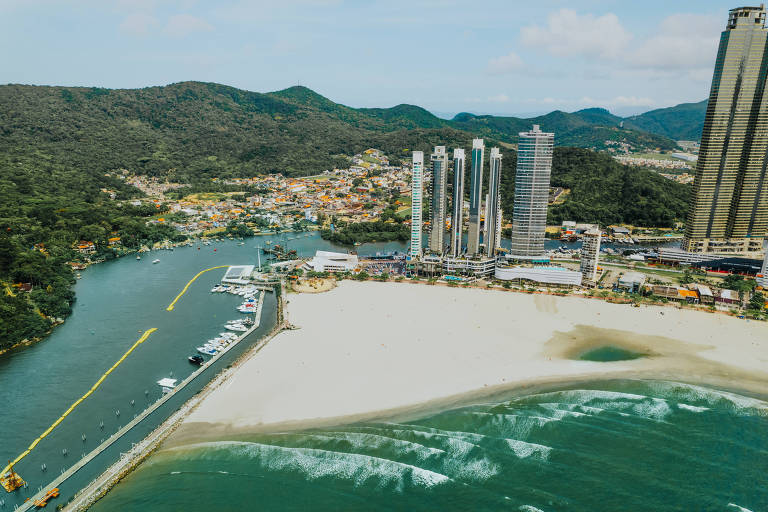 vista aérea de faixa de areia alargada com mar e prédios ao fundo