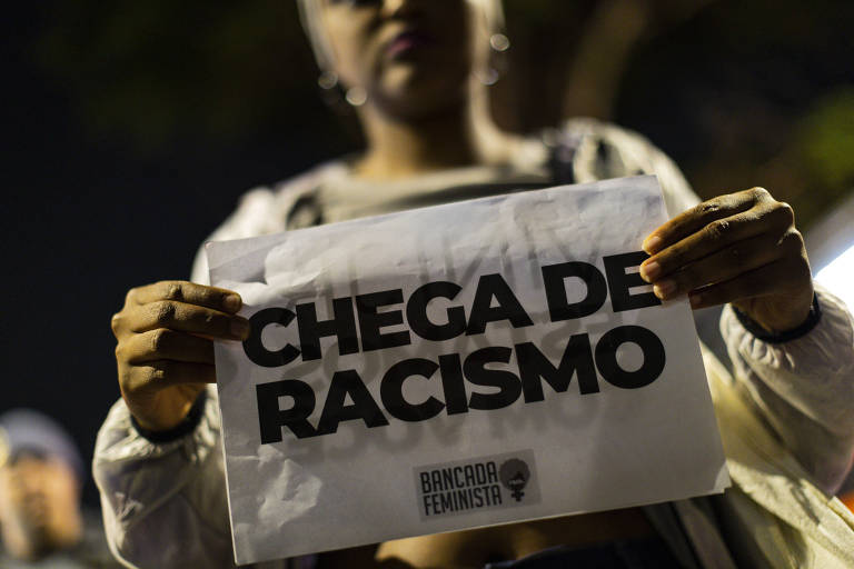 Mulher negra segura cartaz branco onde se lê "chega de racismo"