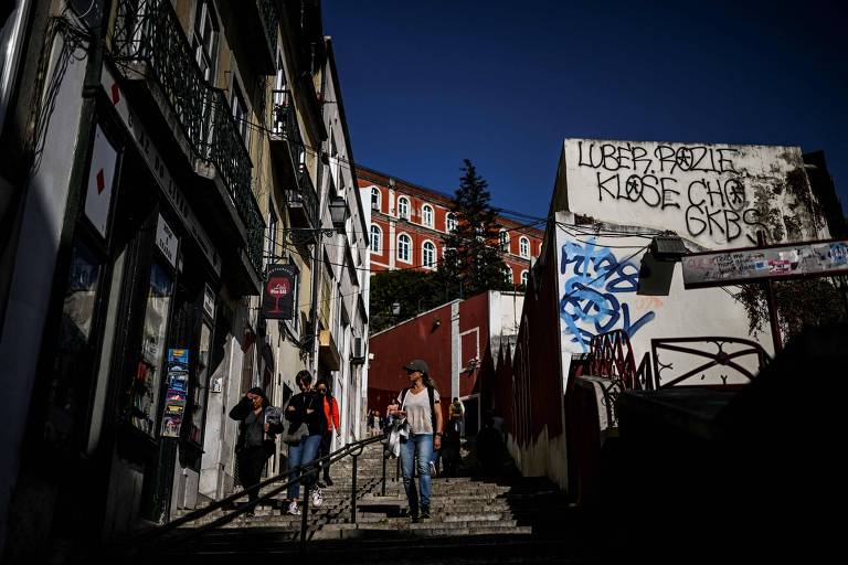 Pessoas caminham em meio a prédios no centro de Lisboa, capital de Portugal, onde reajuste de preços nos aluguéis é de até 6,9% em 2024. Imagem mostra pessoas em uma escada, cercada de imóveis de até 4 andares