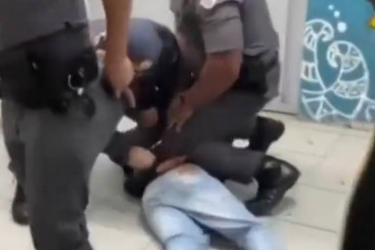 Adolescente aparece no chão sendo contido por dois policiais