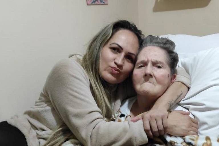 Filha na faixa dos 40 anos abraça a mãe idosa na cama