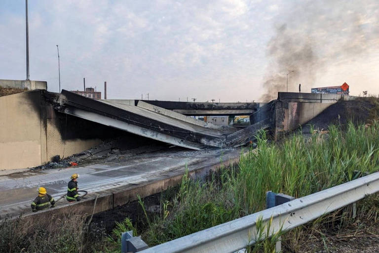 Um trecho de uma rodovia é visto destruído; uma coluna de fumaça sobre da estrutura
