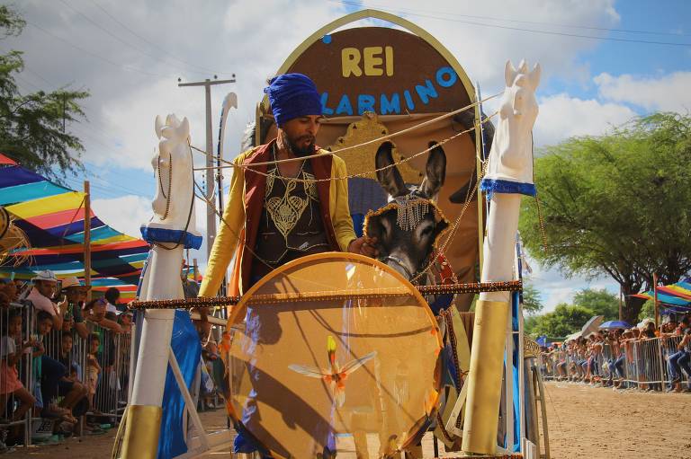 Jegue enfeitado com elementos da cultura africana está dentro de uma carruagem acompanhado do dono que também se veste à caráter.