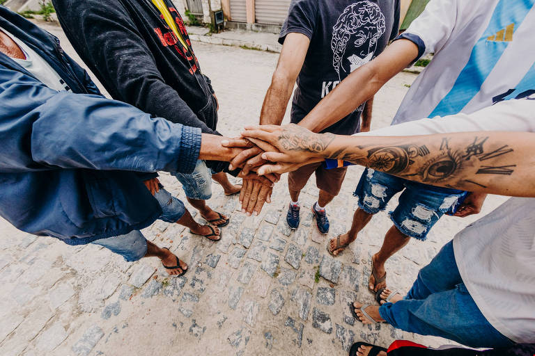 Um círculo de homens juntando as mãos no meio, uma por cima da outra.