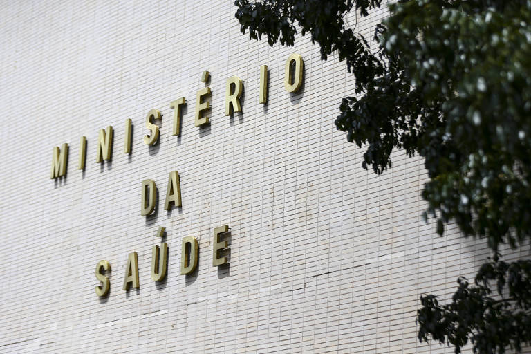 Fachada do Ministério da Saúde, em Brasília. A imagem contém o letreiro escrito "Ministério da Saúde" e uma sobra de árvore no lado direito da imagem. 