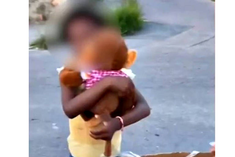 Menina negra, com camiseta amarela, abraça um macaco de pelúcia