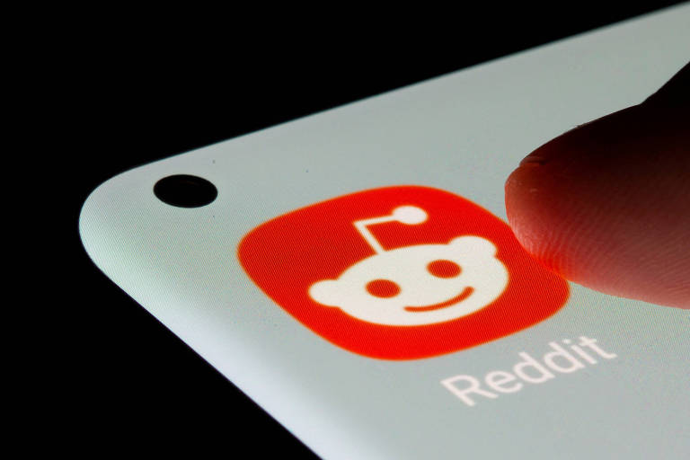 Imagem colorida mostra tela de celular com o ícone do Reddit, uma espécie de robô simpático branco e laranja 