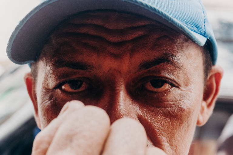 Homem de boné azul e olhar firme cobre parte do rosto com o punho fechado.