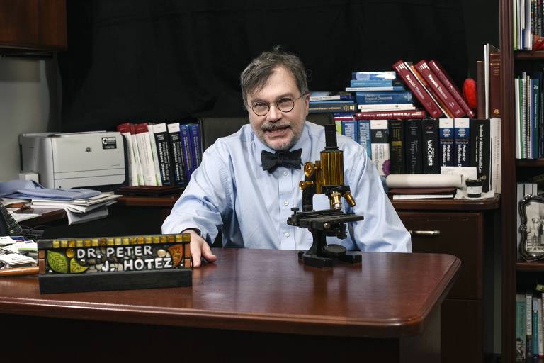 Homem branco, de gravata borboleta, sentado atrás de mesa com microscópio