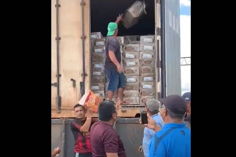 Na imagem, homens pegam pacotes de salsicha dentro de baú de caminhão 