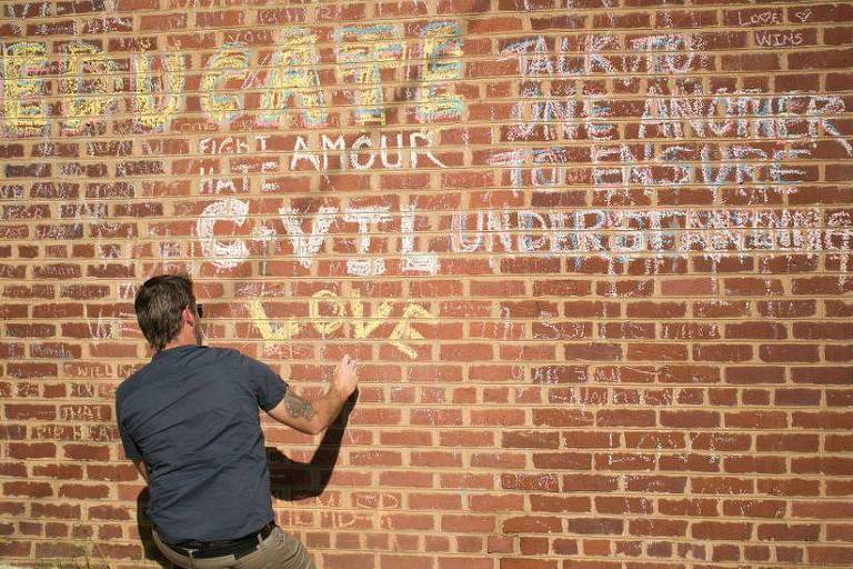 Homem escreve em parede na qual se lê mensagens que pedem compaixão 