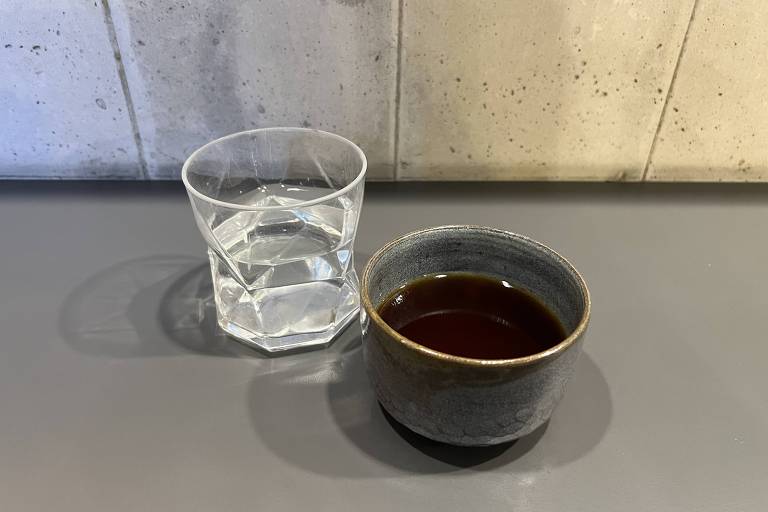 Copo de vidro com água e xícara de cerâmica com café sobre uma bancada