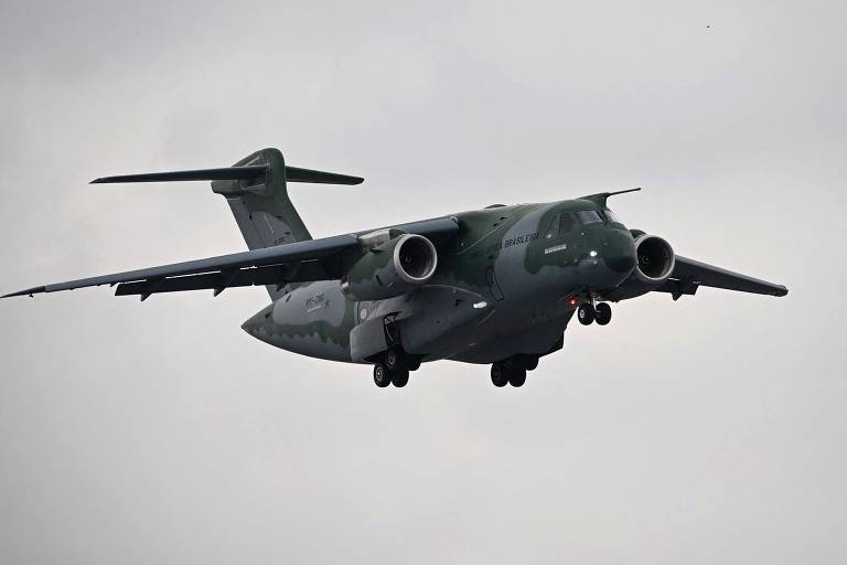Avião militar é capturado por foto durante voo. Ele tem grandes proporções é verde com estampa camuflada.