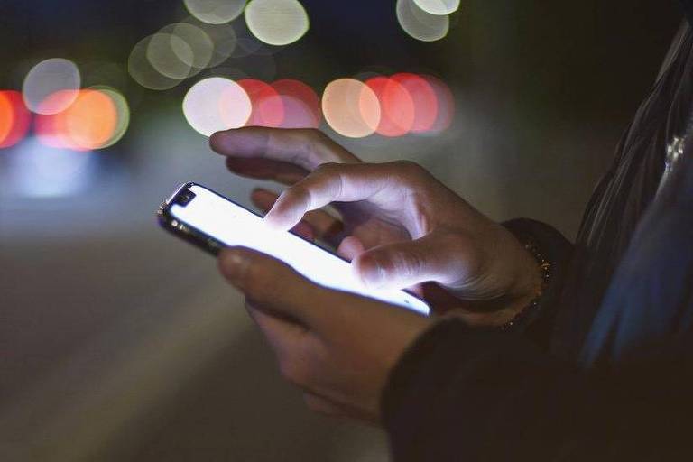 Mão de alguém usando celular na rua à noite
