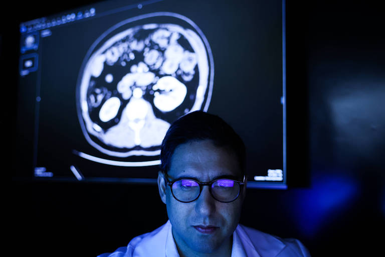Dr Bruno Aragão, medico radiologista responsavel pelo HepatIA, que pesquisa uso de um sistema de inteligência artificial para ajudar a identificar lesões e tumores no fígado no hospital das Clínicas da Faculdade de Medicina da USP. Ele está a frente de uma tela que exibe um exame de imagem.
