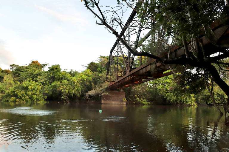 Rio visto a partir de uma margem, passando embaixo de uma ponte de ferro