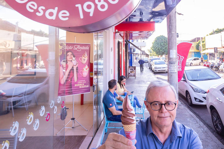 Isaias Bernardes em frente à fachada de sua marca, Chiquinho Sorvetes, segura uma casquinha de sorvete