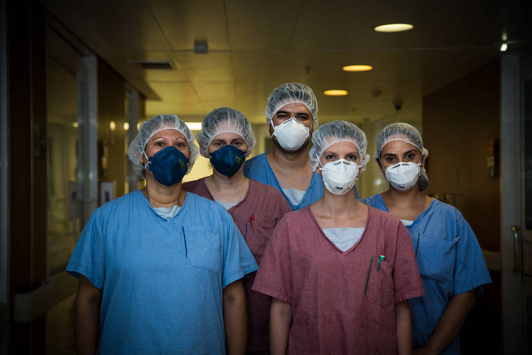 Imagem mostra cinco enfermeiros juntos em corredor de hospital. Eles usam máscara e touca. 