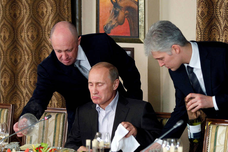 Ievguêni Prigojin (à esq.) auxilia o então premiê russo, Vladimir Putin, durante jantar com acadêmicos e jornalistas estrangeiros no restaurante Cheval Blanc, nos arredores de Moscou, em 2011