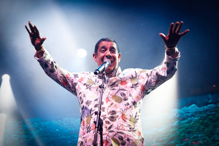 Zeca Pagodinho está de camisa florida e abre os braços durante apresentação no Festival Turá