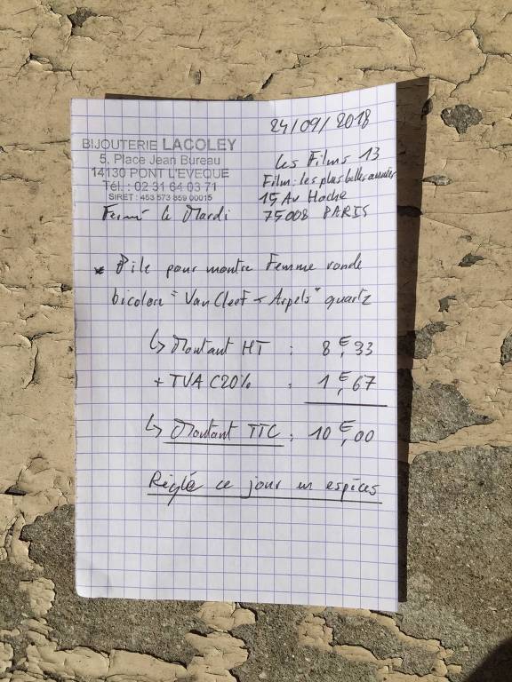 Bilhete em papel quadriculado escrito em francês descrevendo os custos de conserto da troca de bateria do relógio da atriz Anouk Aimée