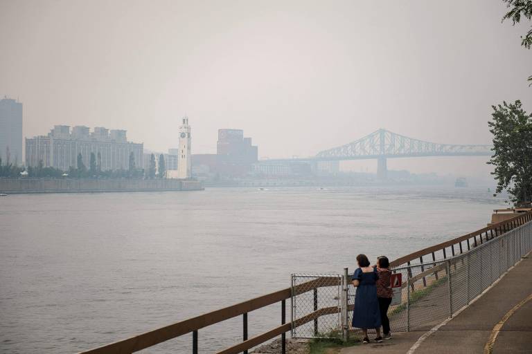 Duas mulheres observam a ponte Jacques-Cartier, em Montreal, ofuscada pela fumaça cinza causada pelos incêndios florestais