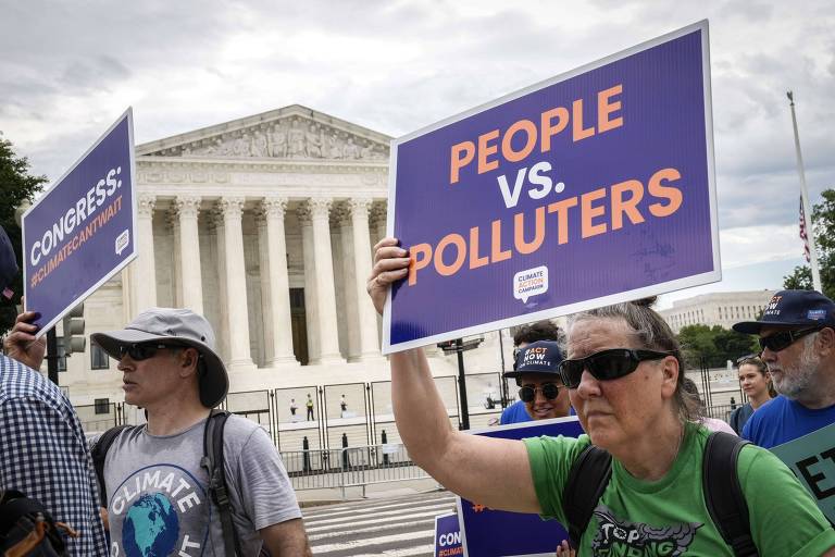 Em meio a grupo de pessoas, mulher segura cartaz dizendo 'people vs. polluters' (pessoas versus poluidores); ao fundo está o prédio da Suprema Corte, um edifício grande com colunas em estilo grego