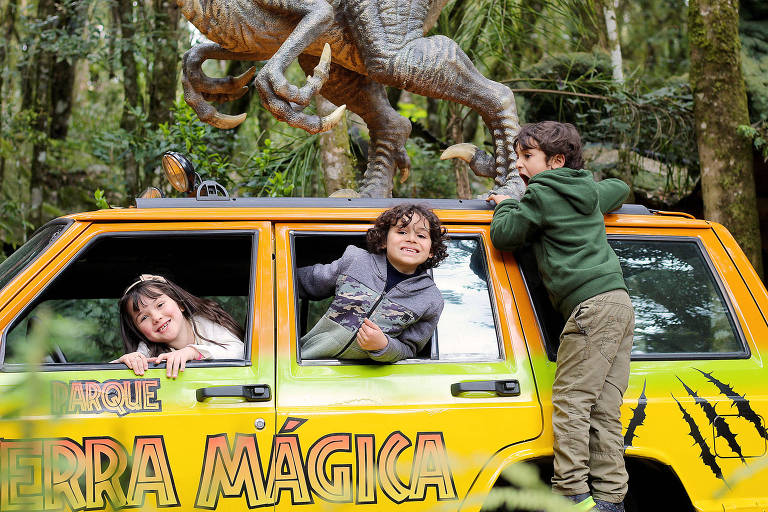 Crianças brincam em carro temático de dinossauros em parque 