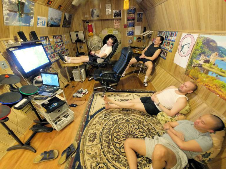 Quatro astronautas sentados numa sala apertada olham para um monitor durante simulação de vida em Marte; eles ficaram isolados por 520 dias em Moscou (RUS)