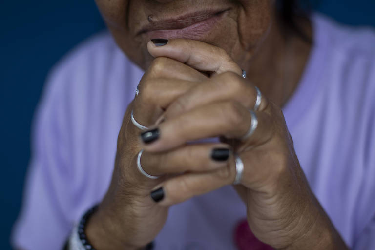 Imagem mostra as mãos pardas, a boca e parte do queixo de uma mulher resgatada de situação análoga à escravidão. Não é possível identificá-la. Ela veste uma camiseta de cor lilás e usa anéis prateados nos dedos das mãos.