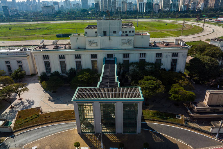 Imagem mostra do alto o pórtico de entrada e, ao fundo, o edifício principal. Atrás dele, está a pista em formato oval e grama ao centro