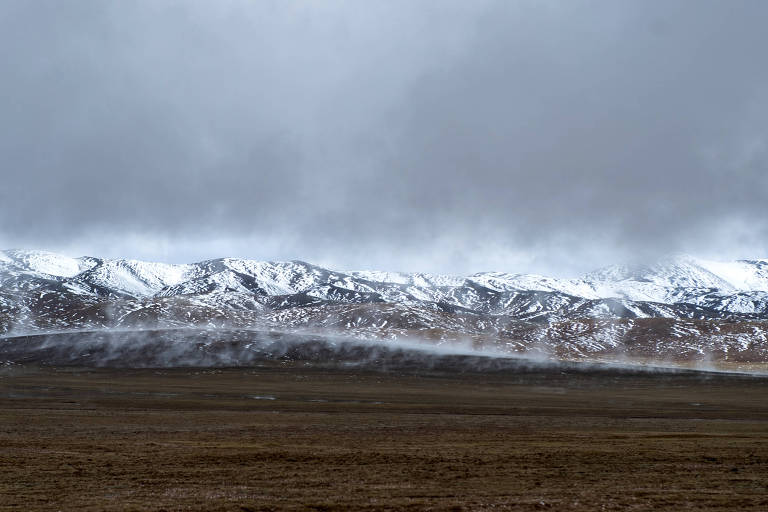 Montanha coberta de neve; à frente há uma planície seca, de cor amarelada