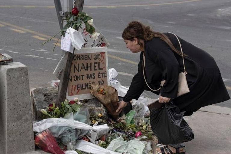 Mulher agachada deposita flores em memorial em calçada