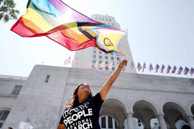 Manifestante ergue bandeira LGBTQIA+ diante da Câmara Municipal de Los Angeles, na Califórnia, durante protesto