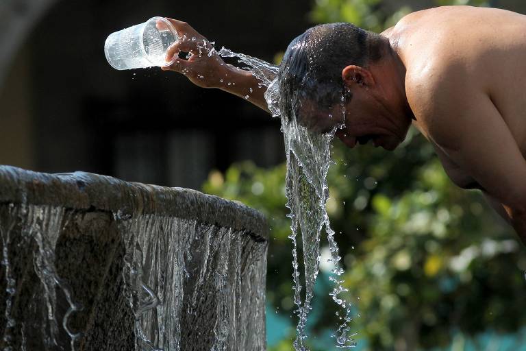 Homem se refresca usando água de fonte em um dos dias mais quentes da terceira onda de calor que atingiu a cidade de Guadalajara, no México
