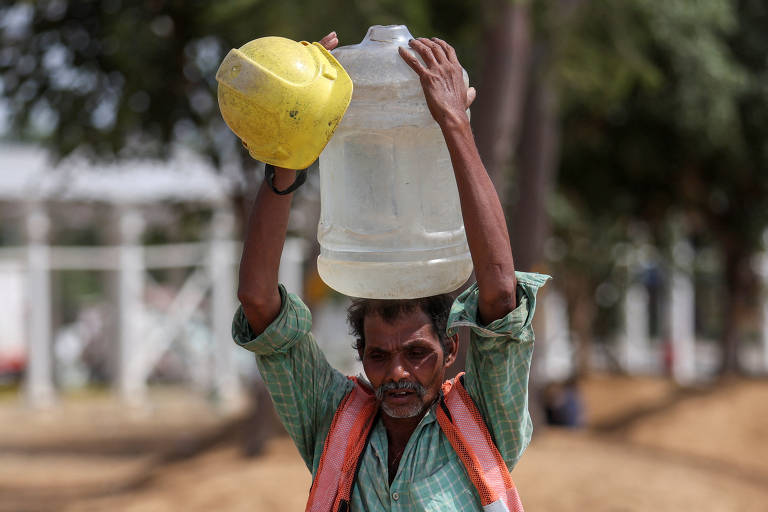 Em dia quente, trabalhador carrega galão cheio com água que vazou de um cano de beira de estrada A labourer carries a container filled with water that leaked from a roadside pipe, em Nova Delhi, na Índia