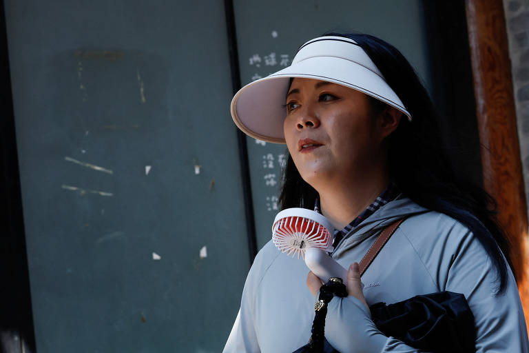 Mulher usa ventilador portátil para se refrescar em meio à onda de calor que atinge a China, em Pequim