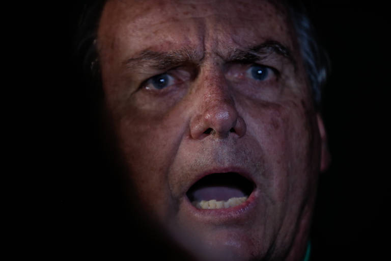 Rosto de Jair Bolsonaro, um homem branco de olhos claros. Ele tem expressão  séria