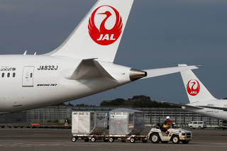 FILE PHOTO: A airport worker drives a luggage transport vehicle past one of the company's Boeing Co's 787 Dreamliner plane and a Beoing 767 at Narita international airport in Narita