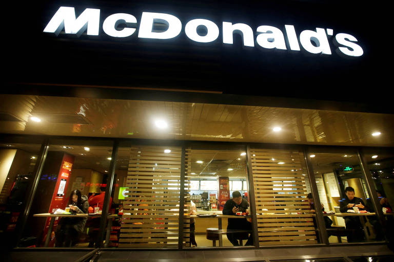 Imagem noturna mostra unidade do McDonald's em Pequim, na China. Clientes estão dentro do restaurante jantando.