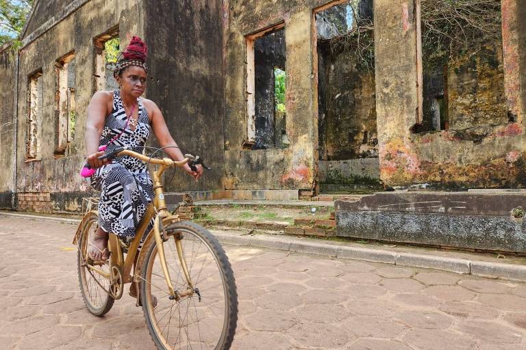 mulher com bicicleta dourada passa por ruínas