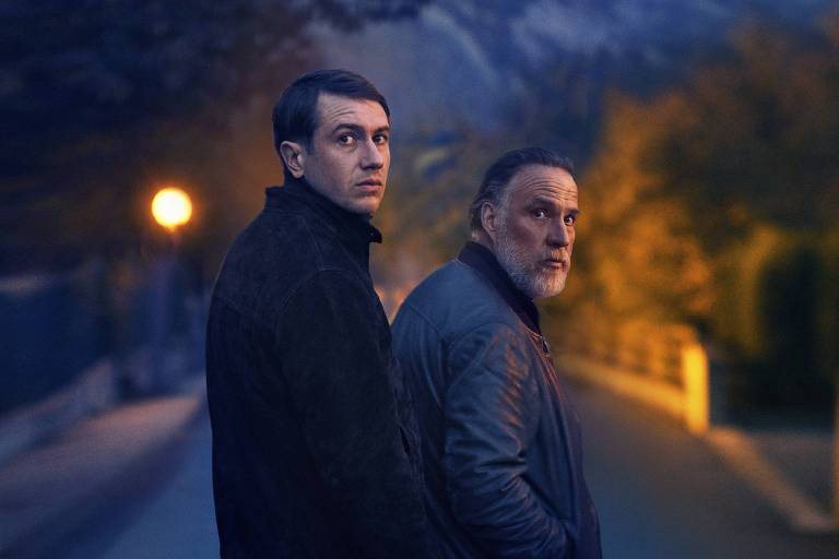 Dois homens brancos olham para trás numa rua escura