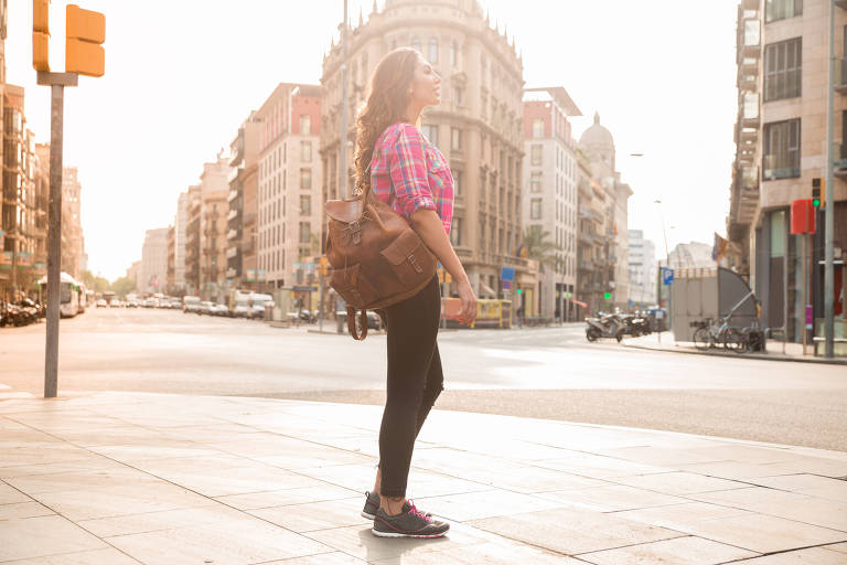 Jovem mulher parada numa calçada de Barcelona contemplando a arquitetura dos prédios