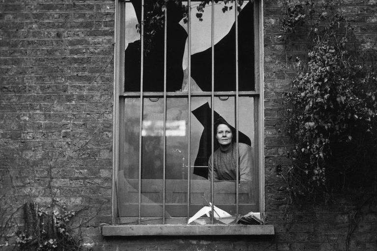 Uma mulher observa através de uma janela quebrada no presídio feminino Holloway, em Londres, depois de um ataque a bomba em dezembro de 1913
