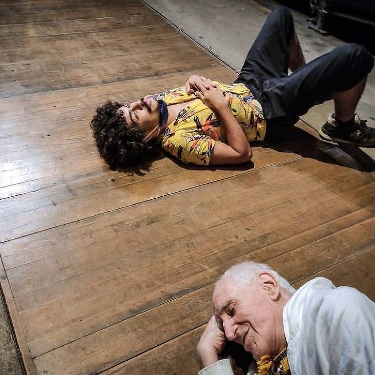 O ator Victor Rosa deitado ao lado do dramaturgo Zé Celso