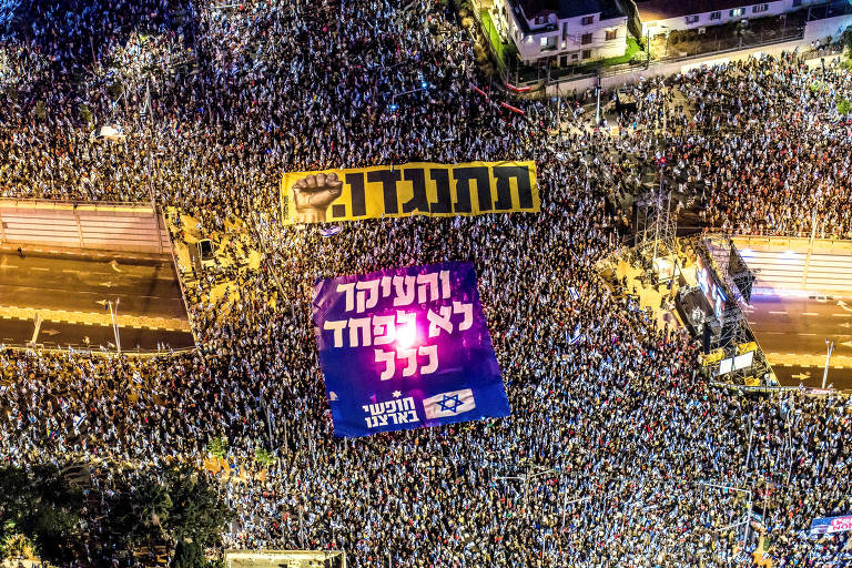 Uma fotografia aérea mostra ruas em Tel Aviv cheias de manifestantes; eles seguram faixas que dizem, em hebraico, "resista" e "o mais importante é não ter medo de jeito nenhum"