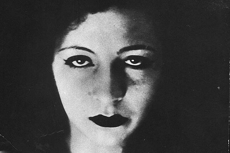 foto em preto e branco antiga mostra mulher de cabelos pretos e traços firmes olhando séria e maquiada para a câmera