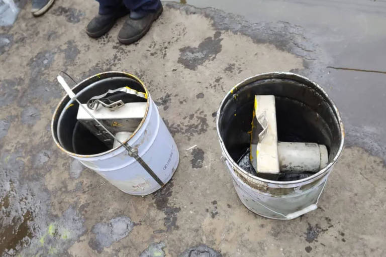 Duas latas brancas sobre um chão de cimento. Dentro das latas, um equipamento branco