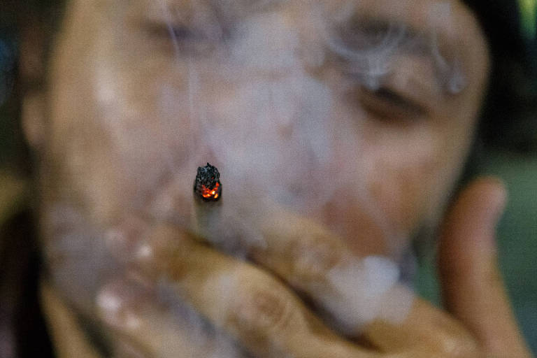 Homem pardo fuma cigarro. A foto destaca o rosto dele e a fumaça que sai do cigarro